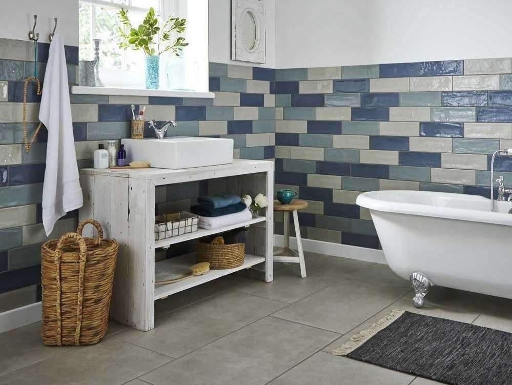 Bathroom wall tiled in blue and grey brick tiles above a grey tiled floor