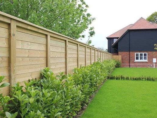 Horizontal timber garden fence with a hedge planted along it